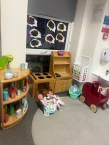 A wooden stove and toys like a pram next to a window