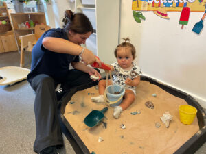 a child playing in a sandpit with an early years practitioner