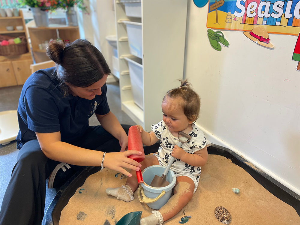 a child playing in a sandpit with an early years practitioner