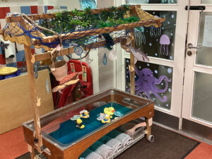 A small water table on wheels with rubber ducks and boat toys in