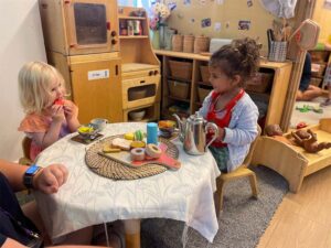 Two children and an early years practitioner sat at a small table having a tea party
