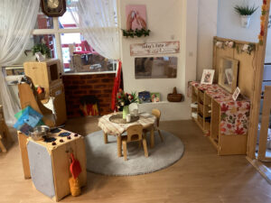 a nursery room with a small table and chairs, toy kitchen appliances like oven and microwave and wooden shelves